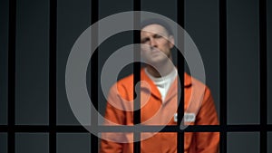 Blurred dangerous prisoner standing behind prison bars, justice, law and order