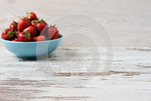 Blurred effect background. Pile of juicy ripe organic fresh strawberries in a large blue bowl. Light rustic wooden background.