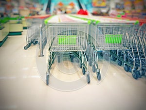 Blurred empty shopping carts green and white handles in a large supermarket;