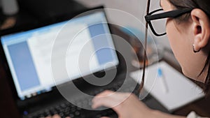 Blurred female hands girl with glasses at night typing on laptop keyboard, looking at screen. Girl freelancer at work