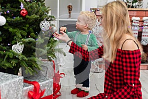 A young mother dresses a Christmas tree with her little son.