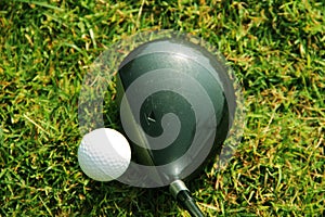 Blurred golf club and golf ball close up in grass field with sunset.