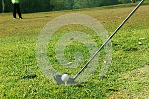 Blurred golf club and golf ball close up in grass field with sunset.