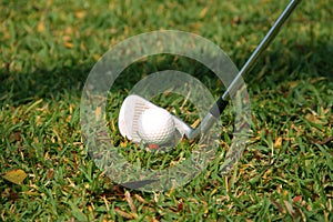 Blurred golf club and golf ball close up in grass field with sunset.