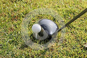 Blurred golf club and golf ball close up in grass field with sunset.