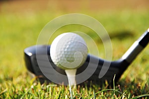 Blurred golf club and golf ball close up in grass field with sunset.