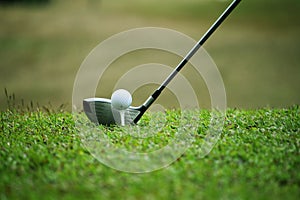 Blurred golf club and golf ball close up in grass field with sunset.