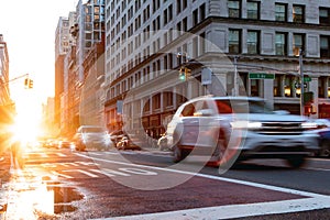 Blurred headlights from cars driving down 23rd Street through Midtown Manhattan in New York City with sunlight background