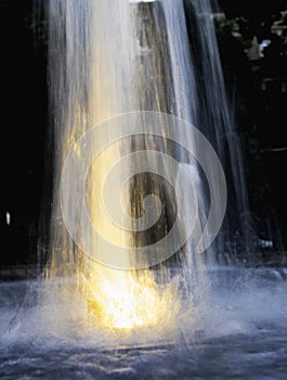 Blurred illuminated fountain spurt, water drops. Droplets - darkness.