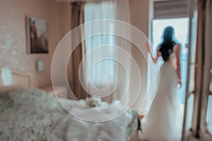 Blurred image for the background. Back view of beautiful brunette bride young woman in the white lace dress near window in the