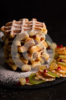 Blurred image of Belgian waffles with powdered sugar and fruits on a dark background