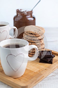 Blurred image of cups of coffee, chocolate chip cookies and chocolate paste in a jar on a light background
