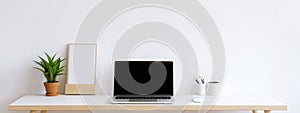 Blurred laptop computer with blank screen on wooden table and white wall background