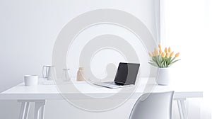 Blurred laptop on a white table with a vase of flowers.