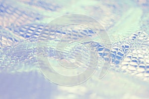 Blurred light rainbow crumpled holographic background with a reptile skin texture in blue toned