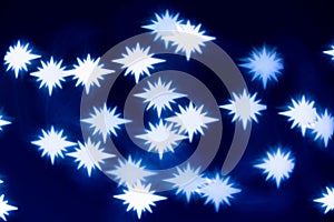 Blurred lights of a christmas garland, bright lights in the form of stars on a blue background, abstract holiday background
