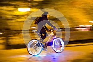 Blurred lights of the city and a silhouette of a cyclist with glowing wheels