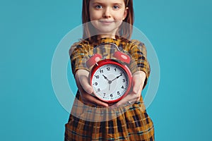 Blurred little kid girl demonstrating red classic alarm clock to camera