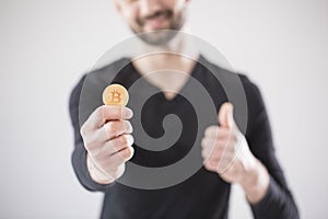 Blurred man in a black T-shirt holding a bitcoin and a thumb up