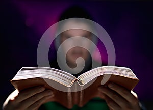 Blurred man on dark background holding a book in his hands