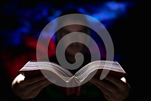 Blurred man on dark background holding a book in his hands