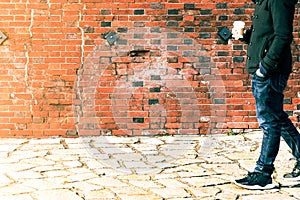 Blurred man walking through a old weathered brick wall hold coffee cup