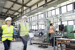 Blurred motion of business people with manual worker in background at industry