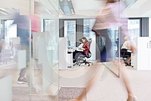 Blurred motion of businesswoman walking with colleagues working in background at office