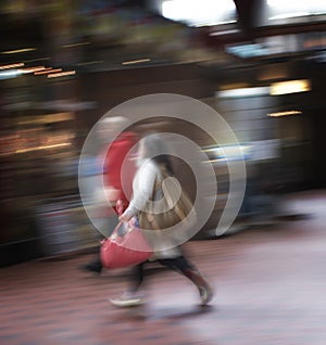 Blurred motion of a couple commuting through an urban town. Man and woman rushing while walking together in a street in