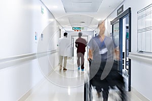 Blurred motion of diverse doctors and medical staff in busy hospital corridor, copy space