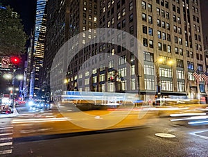 Blurred motion of a yellow taxis driving down the street through New York City at night with building lights in the background