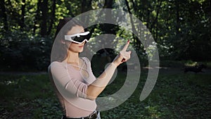 In a blurred nature background, an outdoors game is being played by a young woman in VR glasses