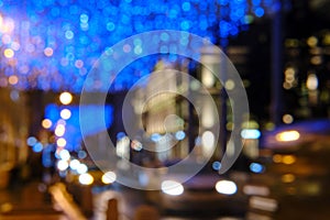 Blurred night city background, festive blue lights and road with cars. Bokeh photo of evening street with holiday cityscape