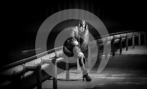 blurred night shot of lonely woman sitting on railings at highway