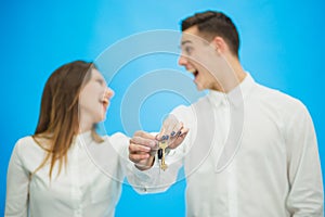 Blurred overjoyed couple with kwys to their new apartments, raising hands up, ready to move as soon as possible. Focus