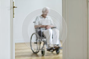 Blurred person in a wheelchair in the background alone at home.