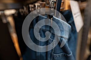 Blurred photo of denim pants in clothing store. Jeans on hanger hanging on rack in clothing store. Fashion retail shop inside