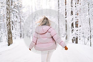 Blurred photo of young blonde woman in winter clothes walking in snowy winter forest