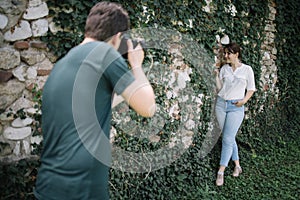 Blurred photographer taking photo session of girl in front of wall with ivy