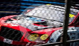 Blurred picture of fence mesh netting and car on racetrack background. Motorsport car racing on asphalt road. Super racing car