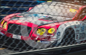 Blurred picture of fence mesh netting and car on racetrack background. Motorsport car racing on asphalt road. Super racing car