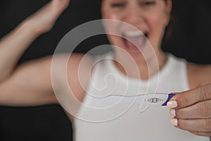 Blurred portrait of happy caucasian woman holding positive express pregnancy test on black background.