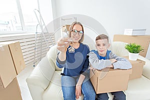 Blurred positive mom and son are sitting on the couch and showing the keys to the new apartment. The concept of home