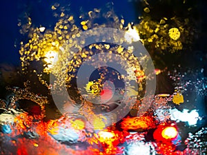 Blurred rain drops on car window with road light bokeh on rainy season abstract background