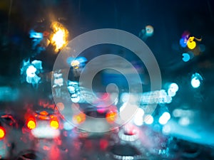 Blurred rain drops on car window with road light bokeh on rainy season abstract background