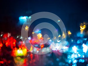 Blurred rain drops on car window with road light bokeh on rainy season abstract background