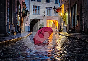 Blurred rainy city street at  evening pink umbrella on wet pavement medieval house street lamp blurred light