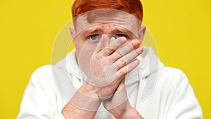 Blurred redhead frightened man rubbing hands posing at yellow background. Scared Caucasian guy having panic attack