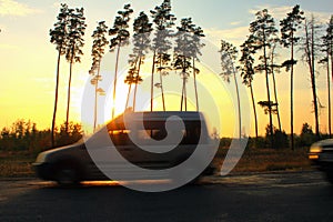 Blurred road and car against the backdrop of sunset and trees, speed motion