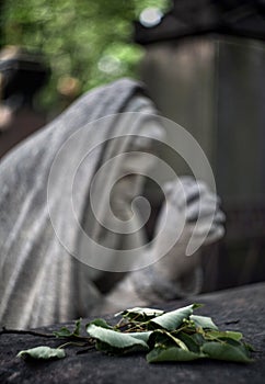 Blurred sculpture of a grieving woman over a grave in with a green leaves in the foreground